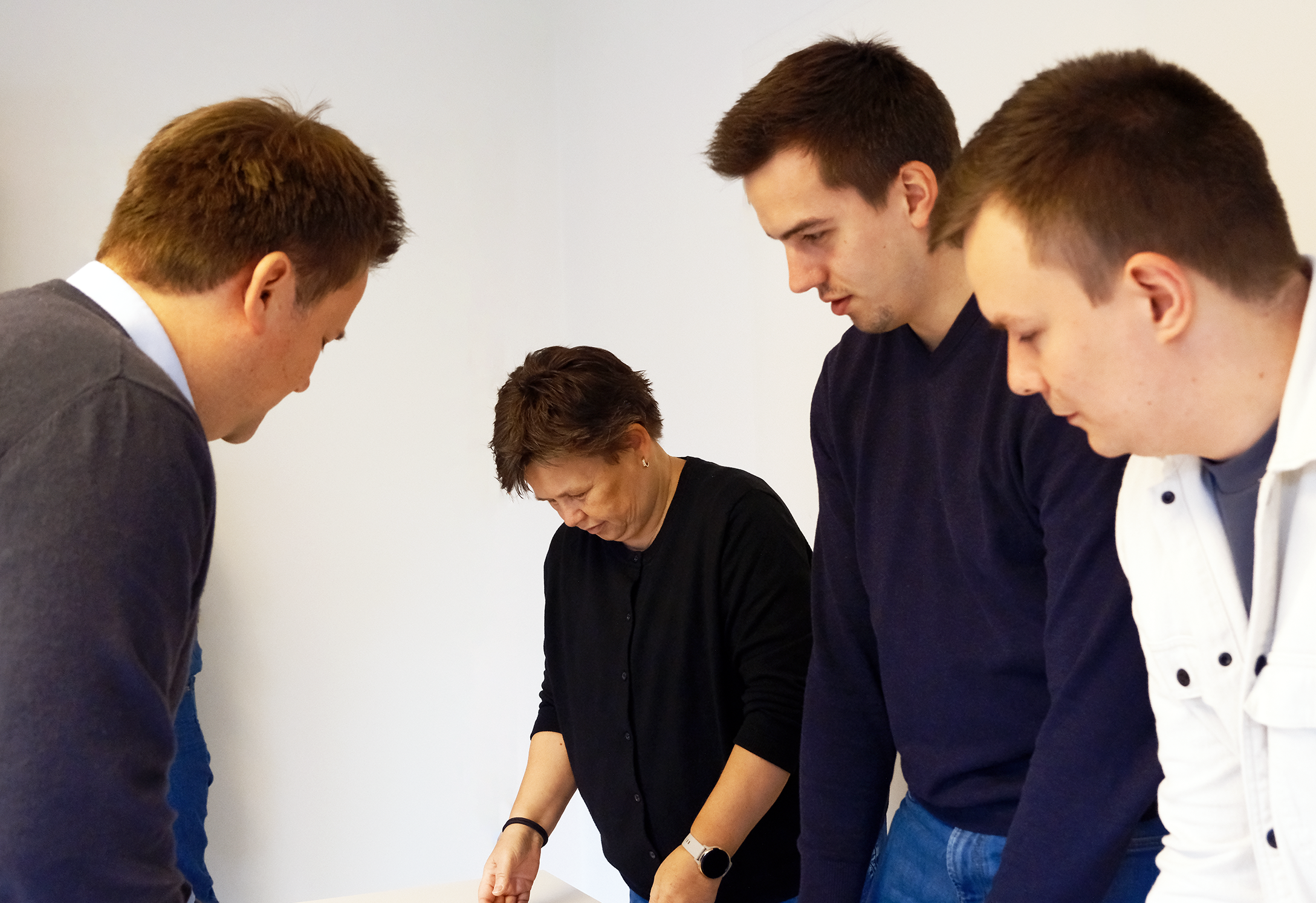 Drei Männer und eine Frau stehen gemeinsam an einem Tisch und sichten Unterlagen - TBE Ingenieurbüro für Tragwerksplanung