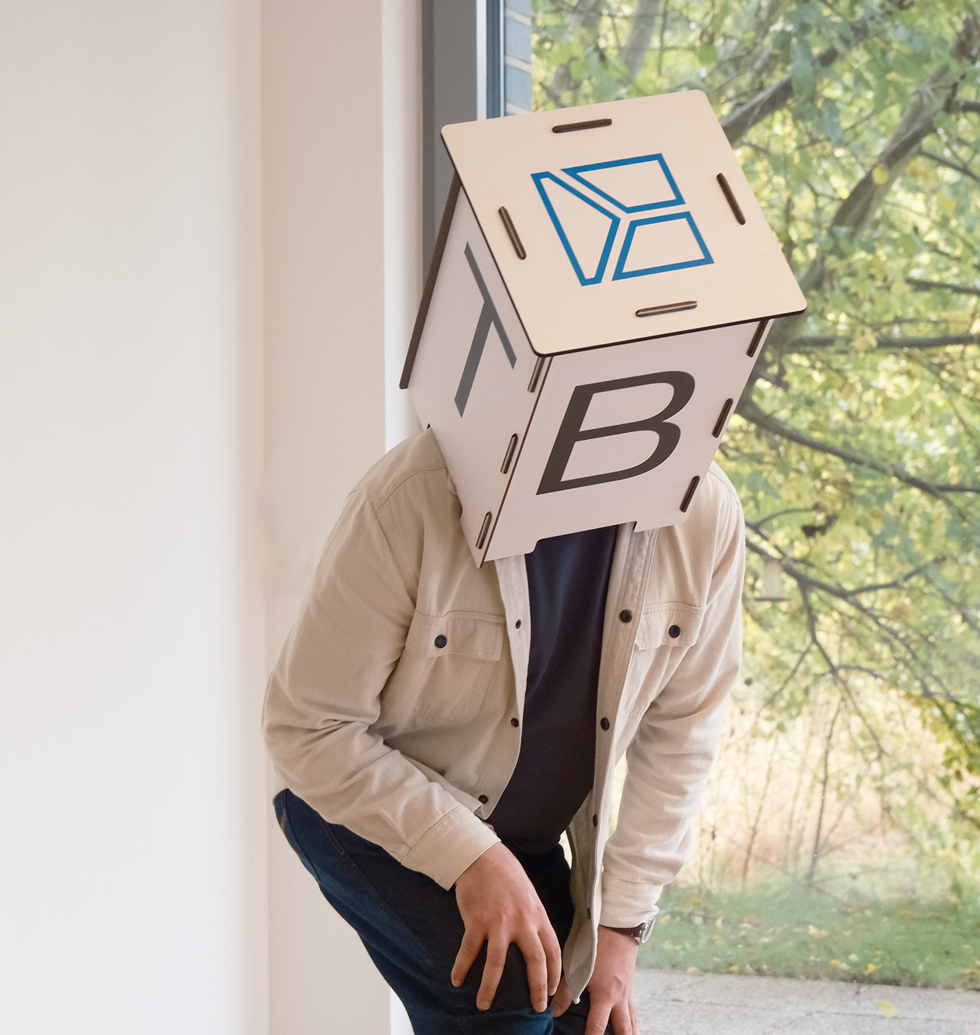 Ein Mann hat einen Kartonwürfel auf dem Kopf mit dem TBE Logo darauf - TBE Ingenieurbüro für Tragwerksplanung