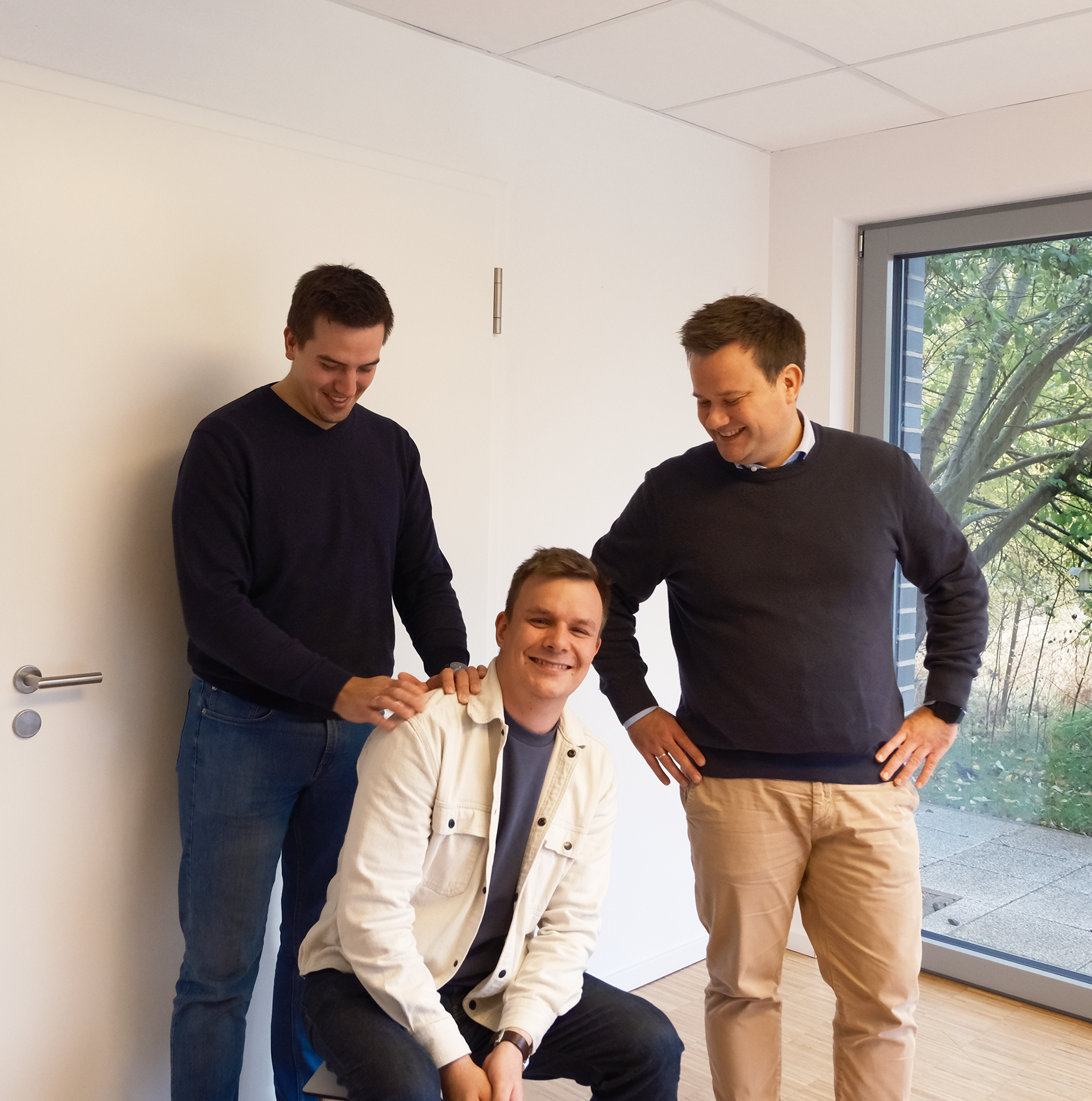 Zwei Männer stehen neben einem Mann der sitzt in einem Raum - TBE Ingenieurbüro für Tragwerksplanung